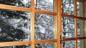 Una ventana de madera con múltiples divisiones, que muestra una vista de árboles cubiertos de nieve.