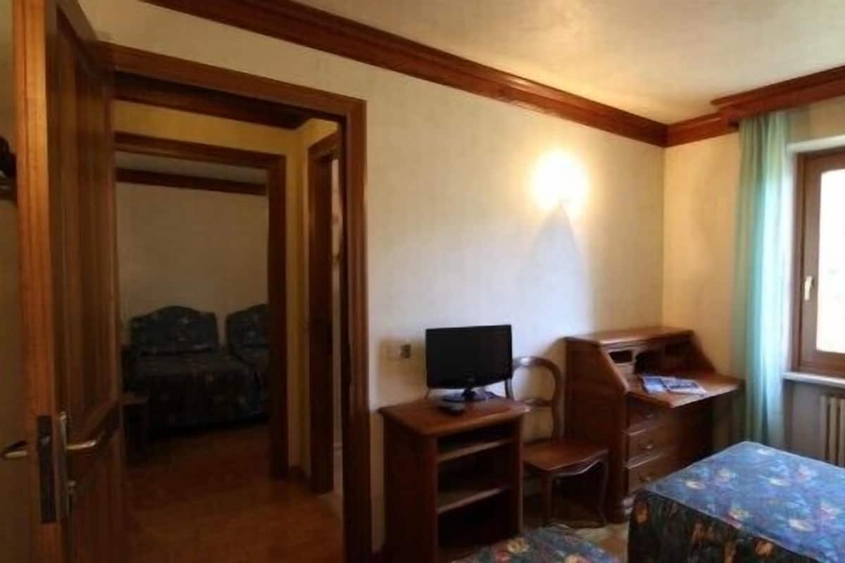 Una habitación con cama, escritorio, silla, televisor y ventana con cortinas.