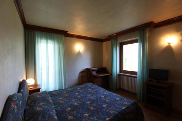 Habitación de hotel con cama, escritorio, silla, televisor y ventana con cortinas.