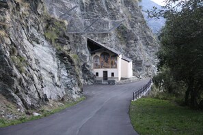 Un camino estrecho que lleva a una pequeña construcción con techo inclinado, rodeada de acantilados rocosos.