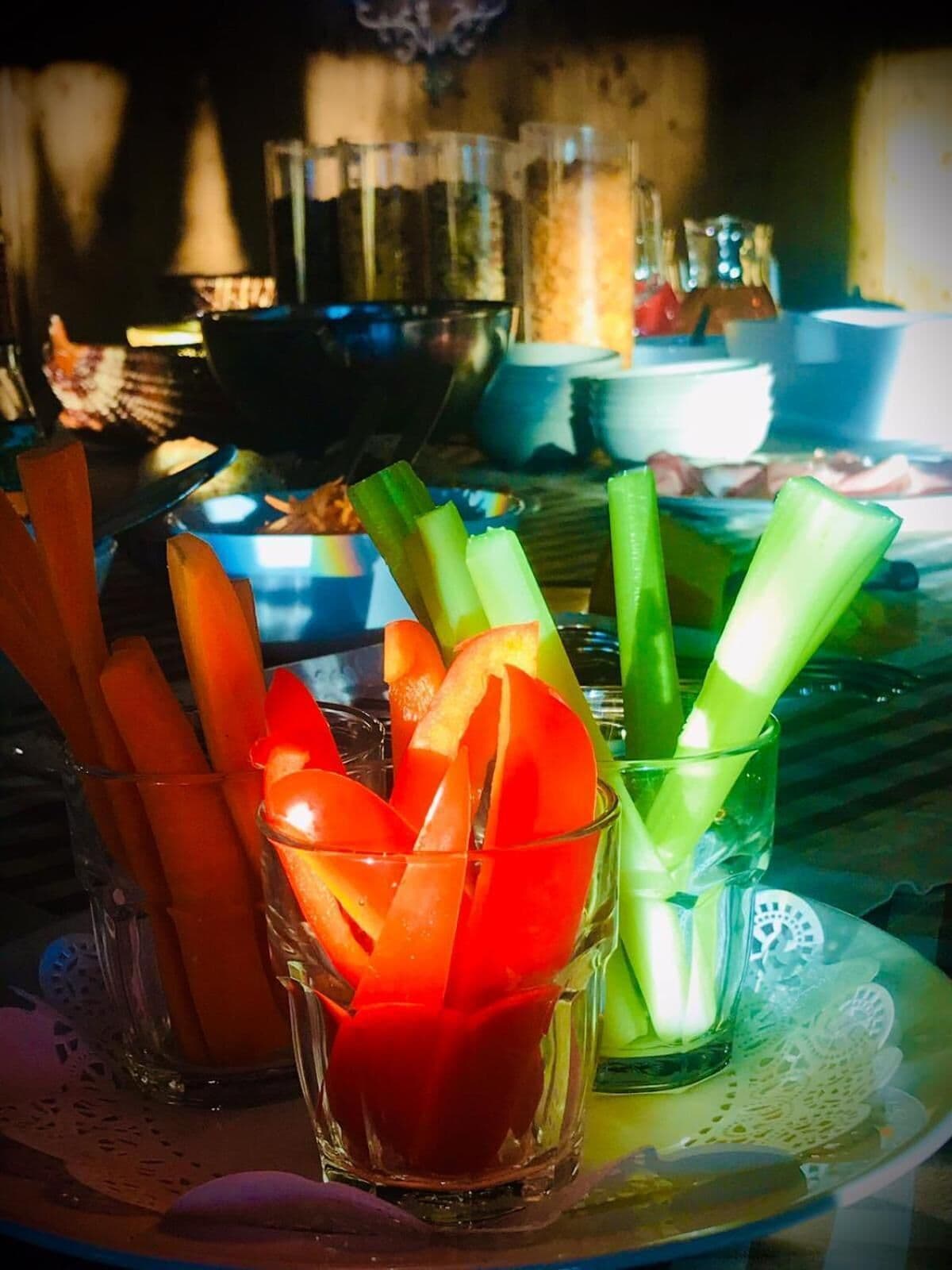 Ein Tisch mit verschiedenen Speisen, darunter Sellerie- und Karottenstifte, sowie ein Glas Wasser.