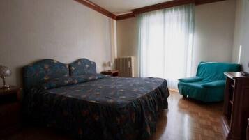 Una camera da letto con un letto grande, una sedia, un termosifone e una finestra con tende.