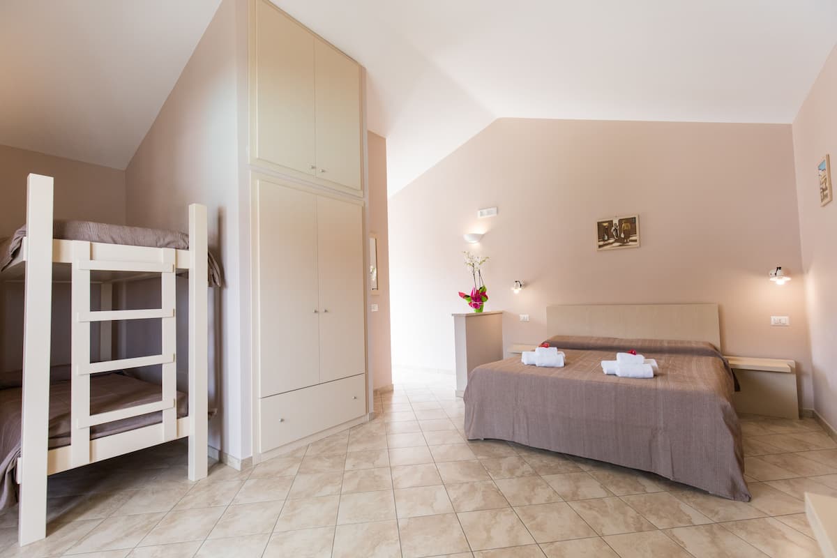 Un dormitorio con literas, un armario amplio, una cama con colcha marrón, una mesita de noche con un florero y luces instaladas en la pared.