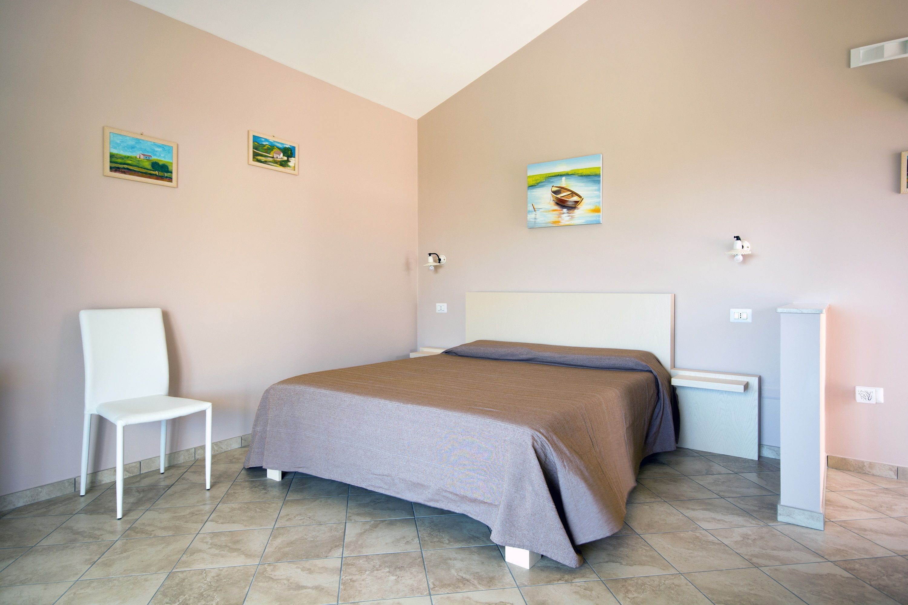 A bedroom with a bed, a chair, and two paintings on the wall.