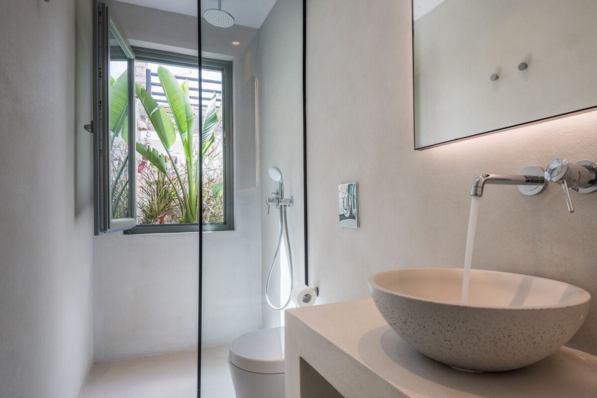 A modern bathroom with a large bowl sink, a handheld showerhead, and a window with a view of plants.