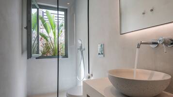 A modern bathroom with a large bowl sink, a handheld showerhead, and a window with a view of plants.