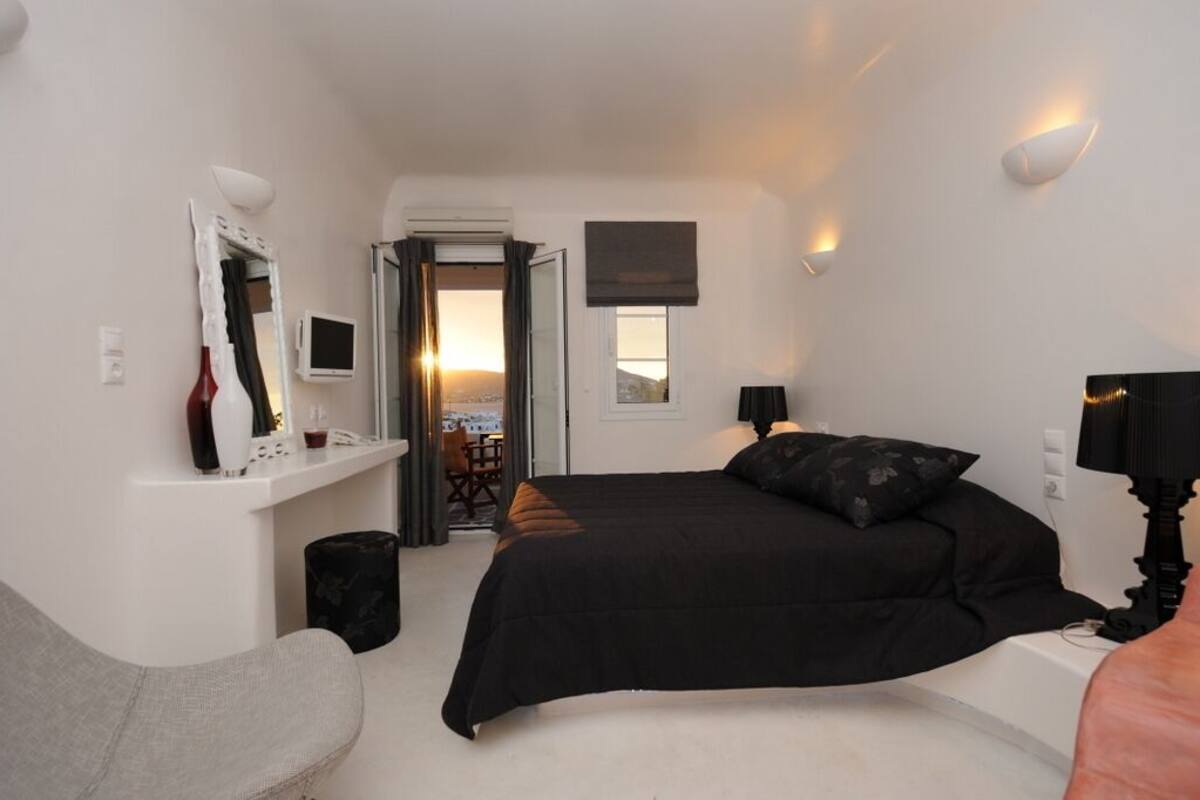 Una habitación de hotel moderna con una cama grande, un escritorio pequeño, una silla, un televisor y vistas de la ciudad a través de la ventana.