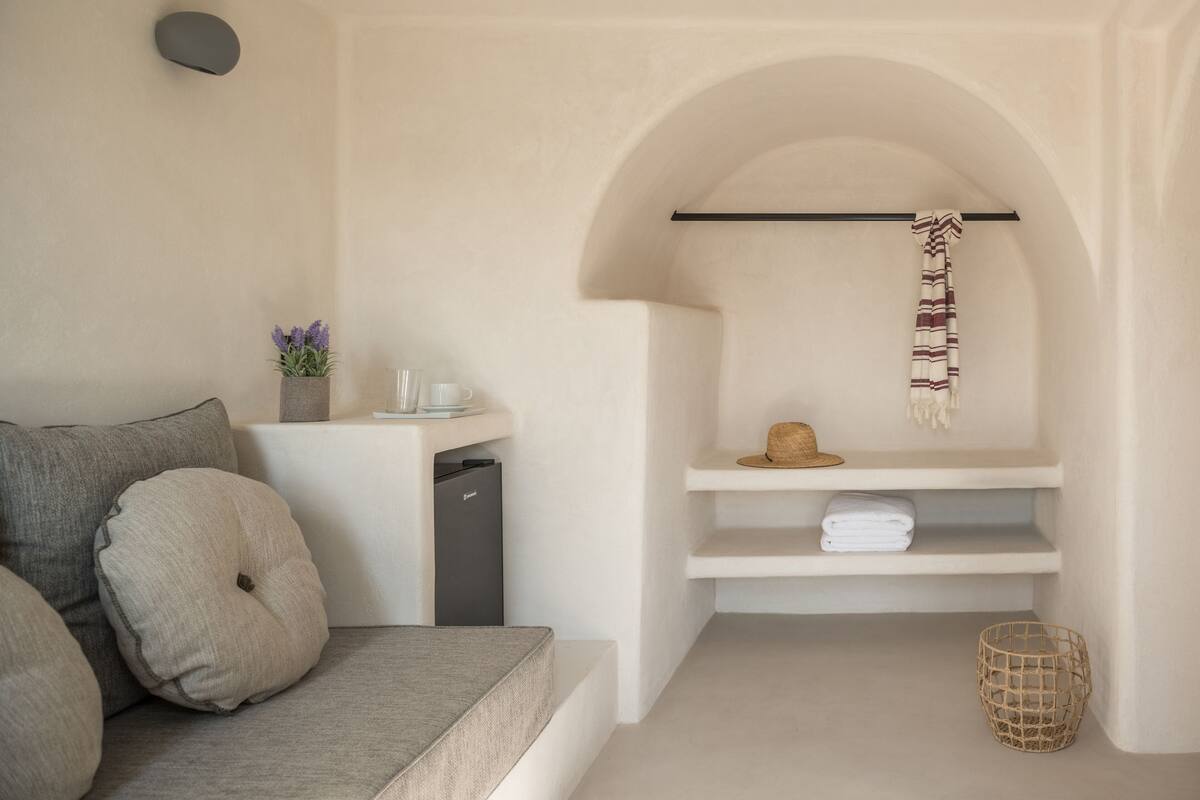 Una habitación moderna y minimalista con sofá, una mesita con un florero, estante con toallas dobladas y una cesta.