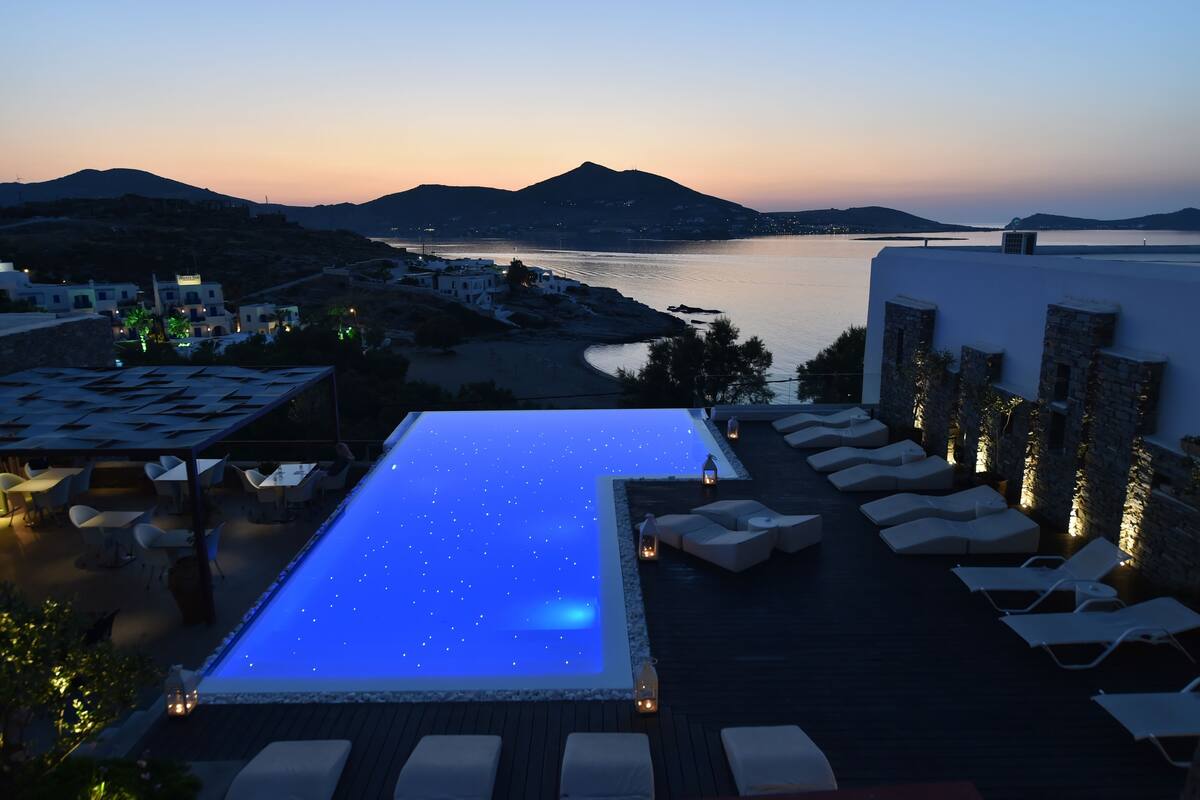 Una piscina infinita en la azotea con vista al mar y a las montañas, sillas de descanso y zona de comedor al aire libre.