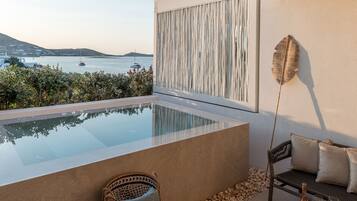 A modern outdoor lounge area with a pool, seating, and a view of the sea.