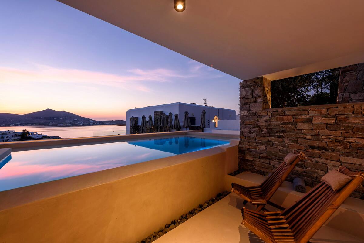 Una piscina en la azotea con vista a una montaña y una masa de agua al atardecer.