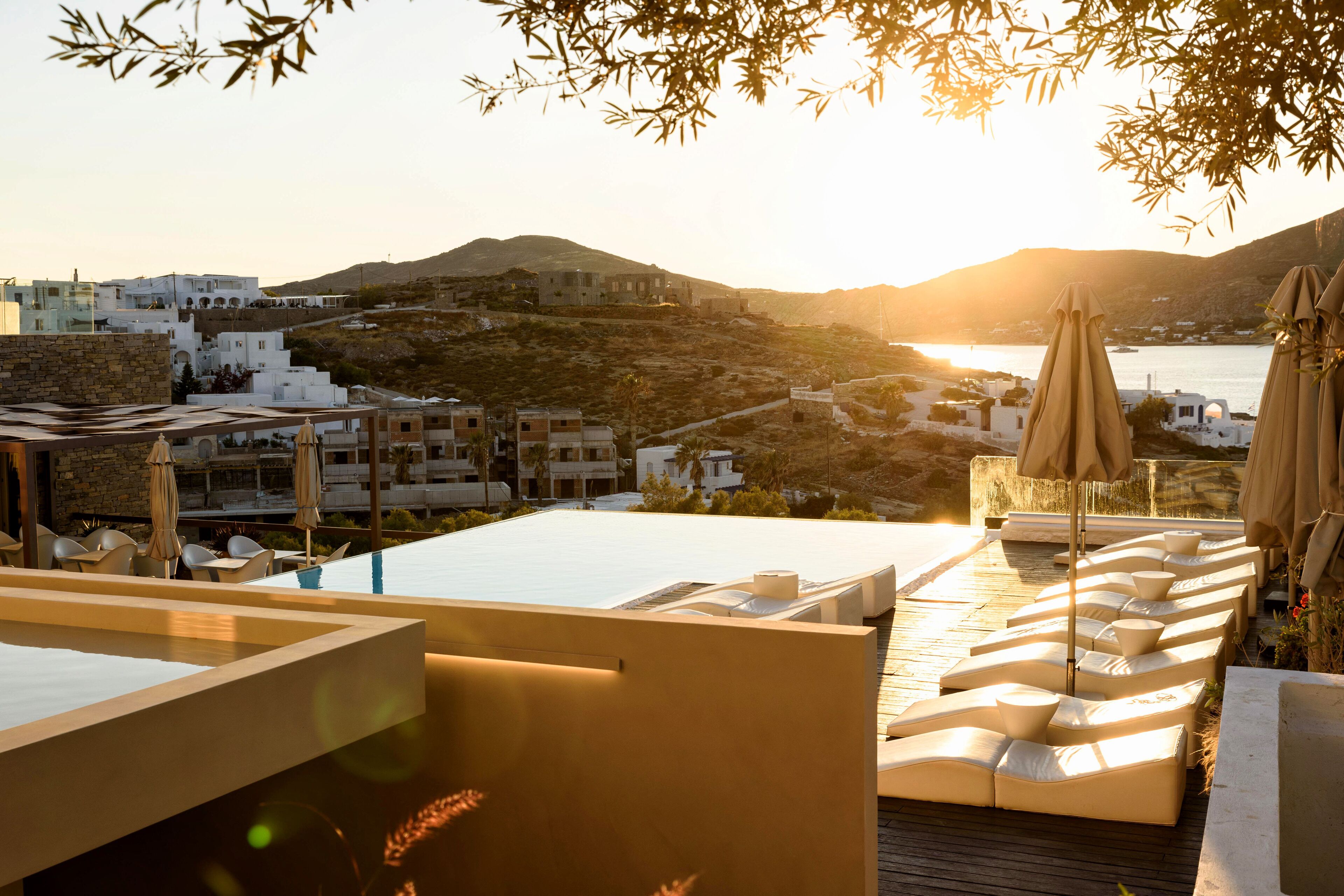 Terraza en la azotea con sillones de descanso y sombrillas, con vistas a un pueblo costero y al mar.