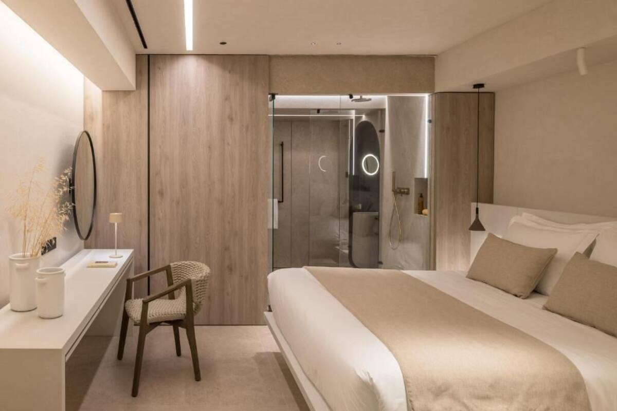 Un dormitorio moderno con una cama grande, un escritorio y una silla. Hay una puerta de vidrio que da al baño.