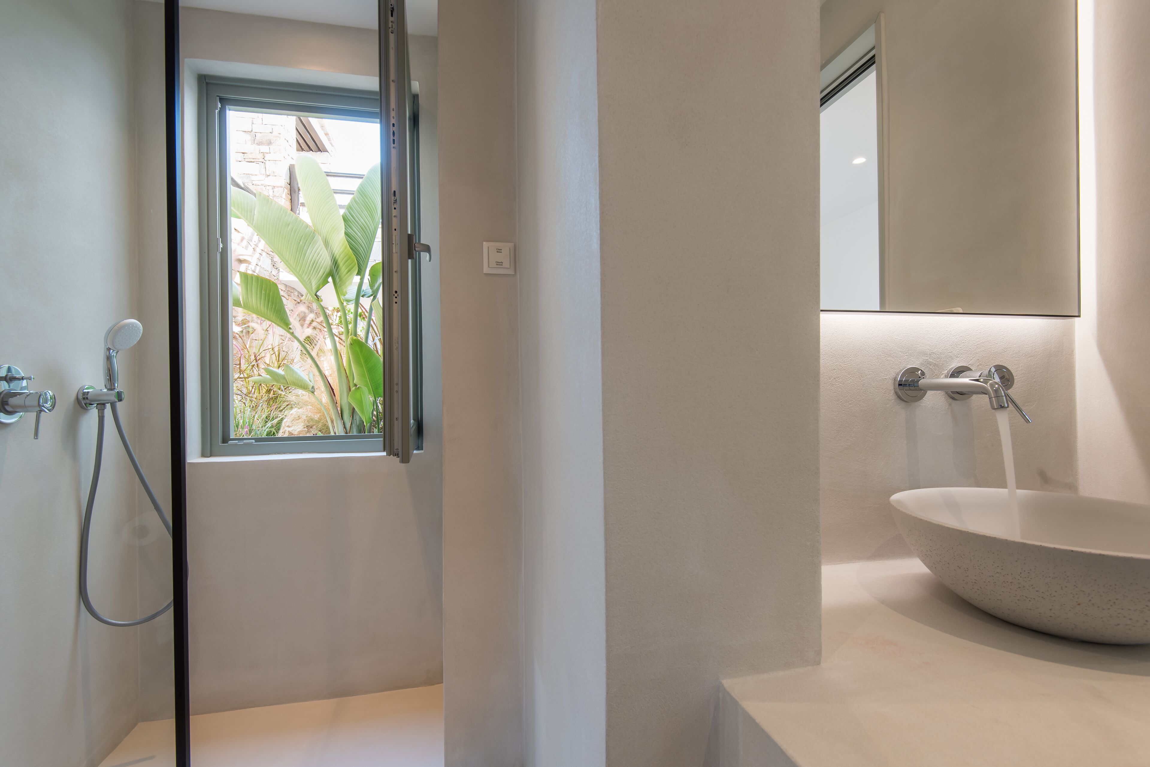 Un baño moderno con un amplio ventanal, ducha separada y lavamanos sobre encimera.