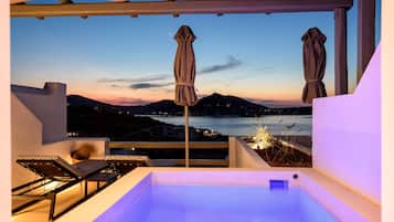 A rooftop terrace with a hot tub, lounge chairs, and umbrellas overlooking a coastal view.