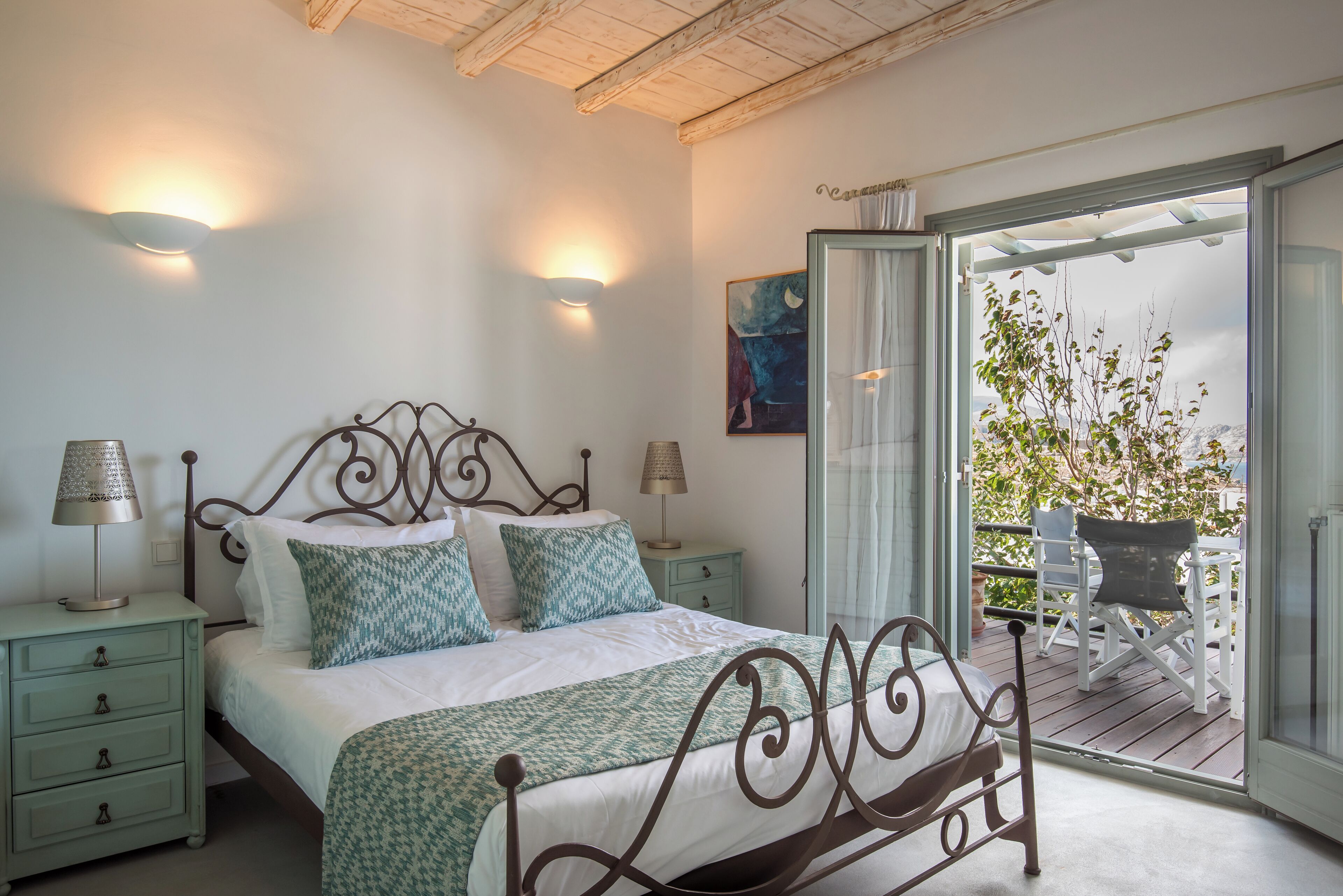 Un dormitorio con una cama, dos mesitas de noche con lámparas, una ventana con cortinas y vistas a una terraza.
