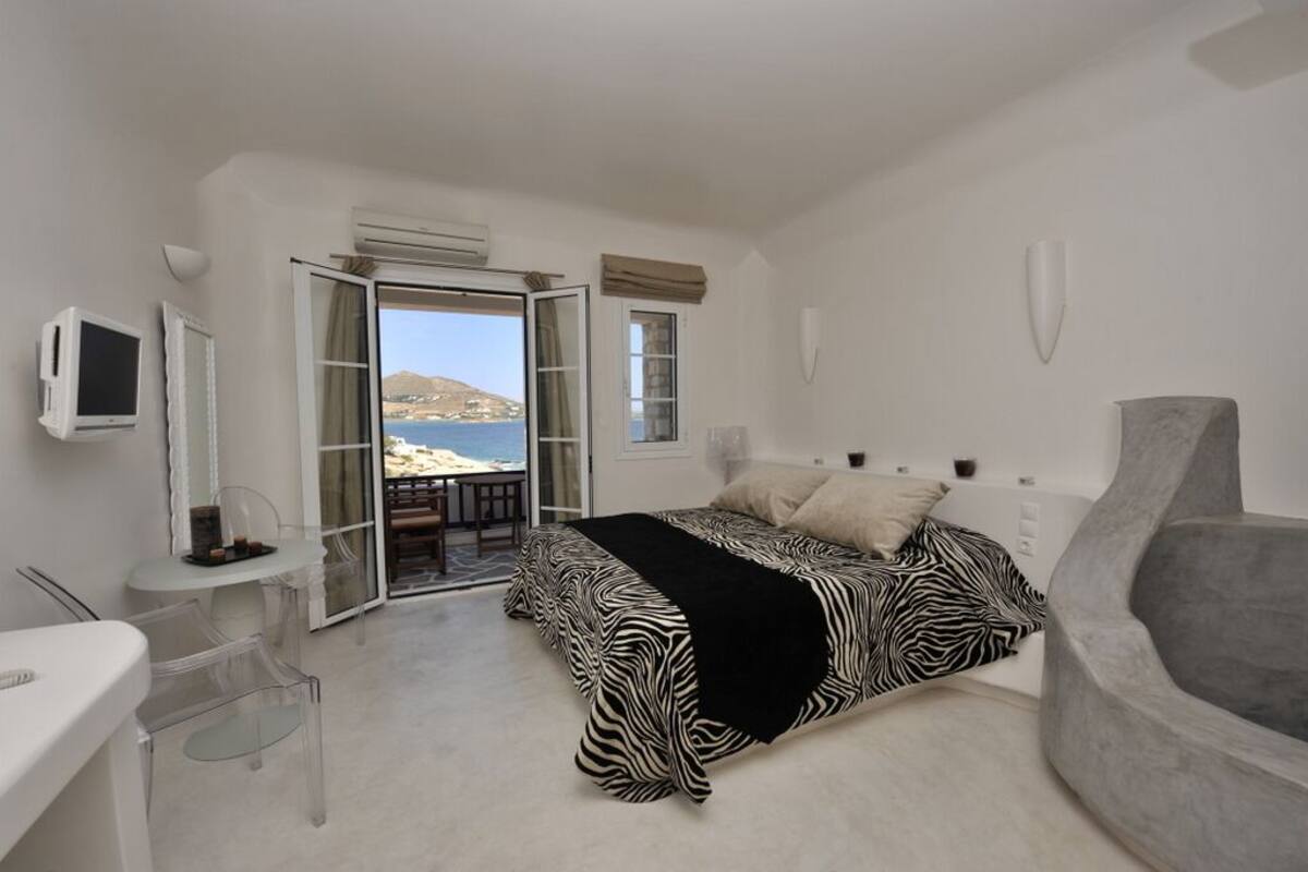 Un dormitorio con cama, escritorio, silla y vista al mar.