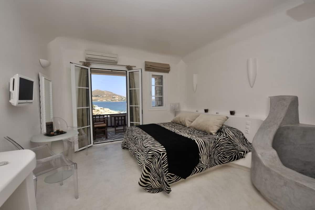 Une chambre avec un lit, un bureau, une chaise et une vue sur la mer.