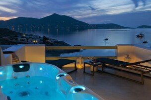 A hot tub with a view of a calm sea and distant mountains at dusk.