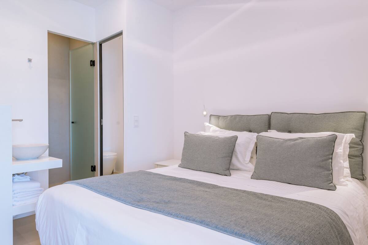 Un dormitorio moderno con una cama grande, una mesita de noche y una estantería empotrada con toallas dobladas.