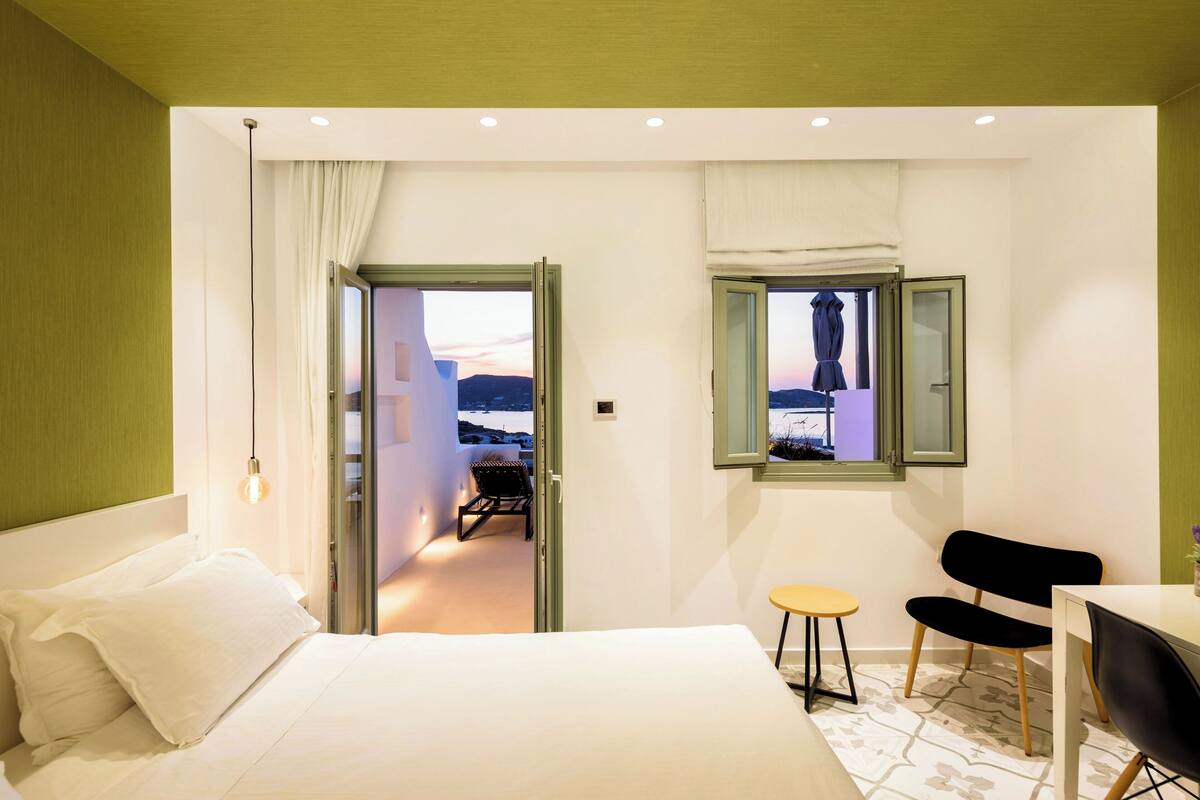 Habitación de hotel con cama, escritorio, dos sillas y ventana con vistas.