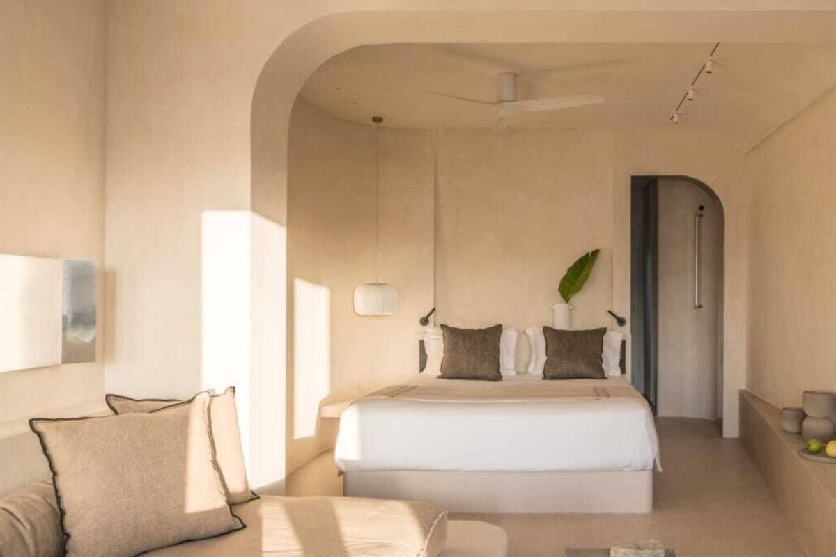 Un dormitorio moderno con una cama grande, un sofá, un espejo y una planta.