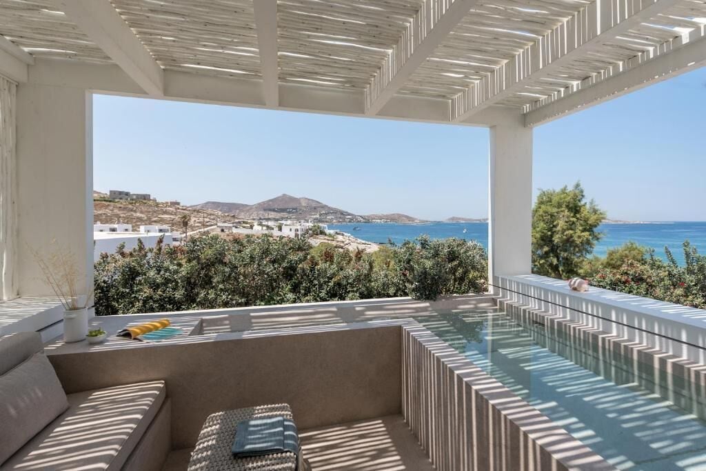 A modern outdoor seating area with a pool, overlooking a coastal landscape.