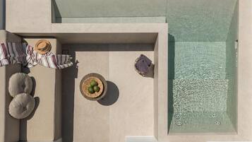 An aerial view of a modern outdoor pool area with a hot tub, lounge chairs, and a small table with a basket.
