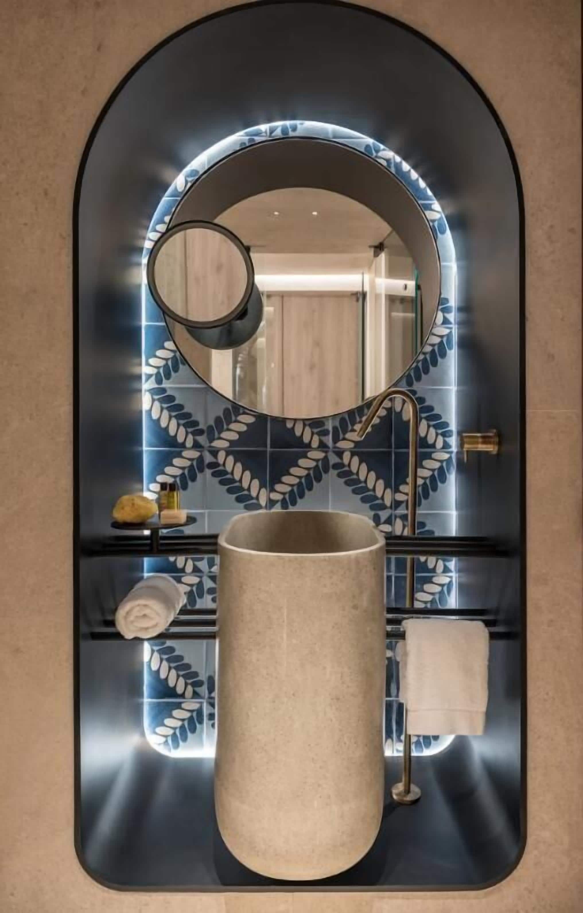 Un baño con un espejo redondo, un lavamanos y un perchero para toallas.