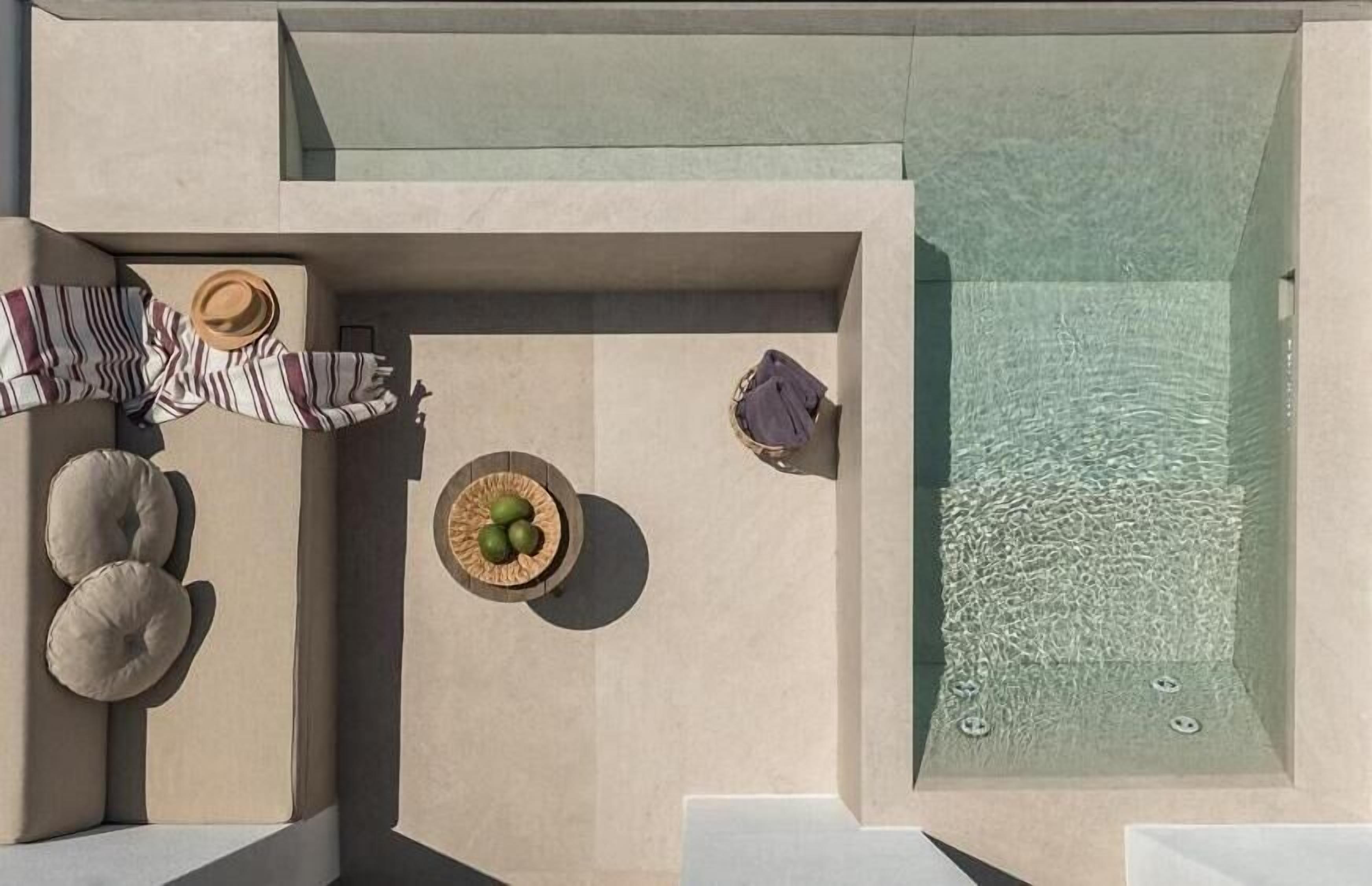 An aerial view of a modern outdoor pool area with lounge chairs, a small table with a basket, and a hot tub.