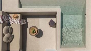 An aerial view of a modern outdoor pool area with lounge chairs, a small table with a basket, and a hot tub.