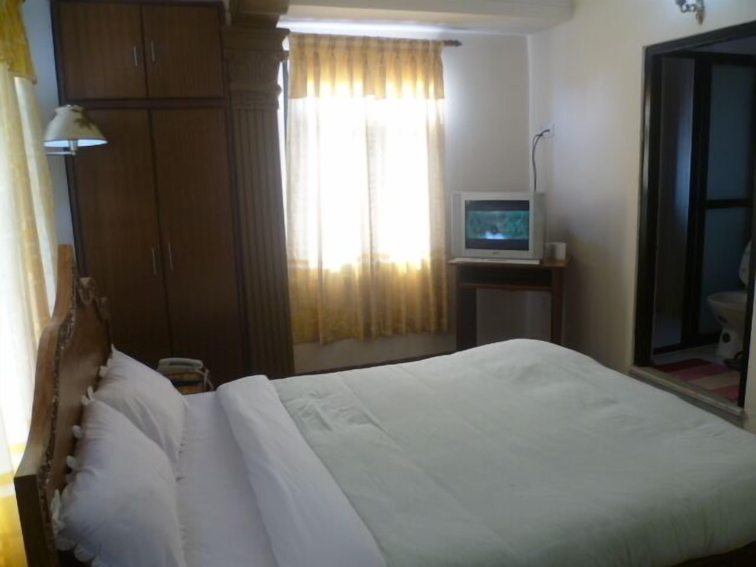 A hotel room with a bed, a television on a small table, and a wardrobe.