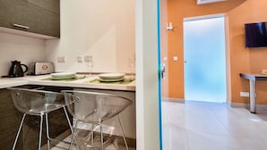 A modern kitchen with a dining area, clear chairs, a flat-screen TV, and a door leading to another room. - Jules Suites (St. Julian's)