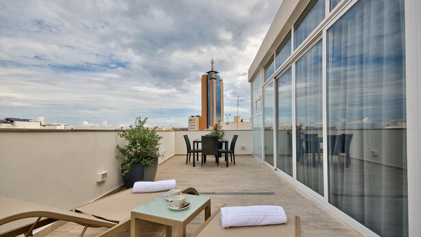 A rooftop terrace with a table and chairs, a potted plant, and a view of a tall building. - Jules Suites (St. Julian's)