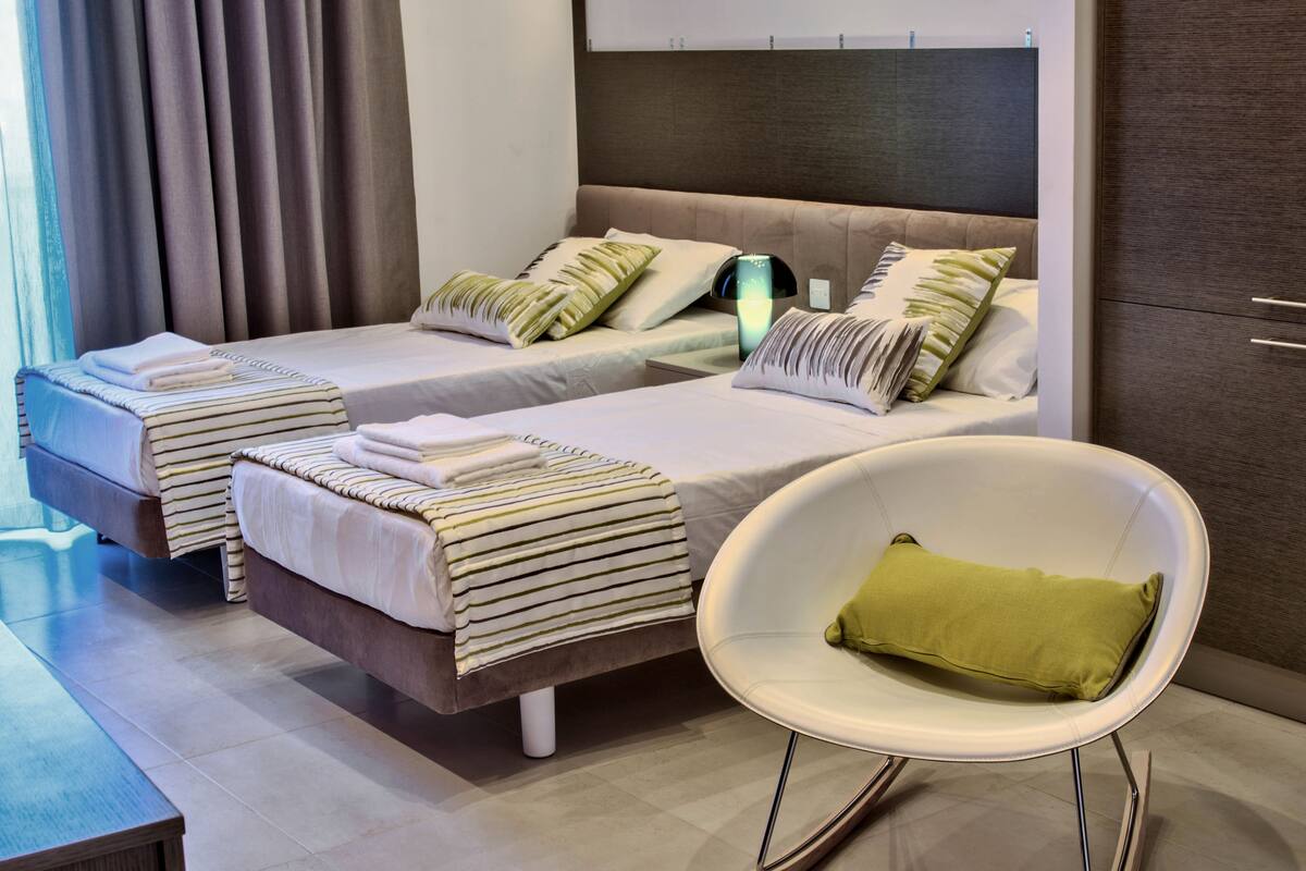 A hotel room with two beds, a bedside table, a chair, and a wardrobe.