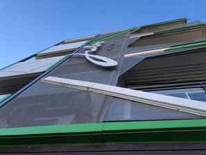A modern building with a prominent curved structure and a green base. - Jules Suites (St. Julian's)