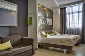 A modern hotel room with a large bed, a sofa, and a wall-mounted TV. - Jules Suites (St. Julian's)