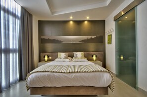 A modern hotel room with a large bed, a cityscape mural on the wall, and a glass door closet. - Jules Suites (St. Julian's)