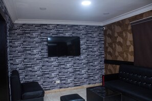 Una habitación con pared de diseño de piedra, un televisor de pantalla plana montado sobre un sofá de cuero negro y un sillón de cuero negro.