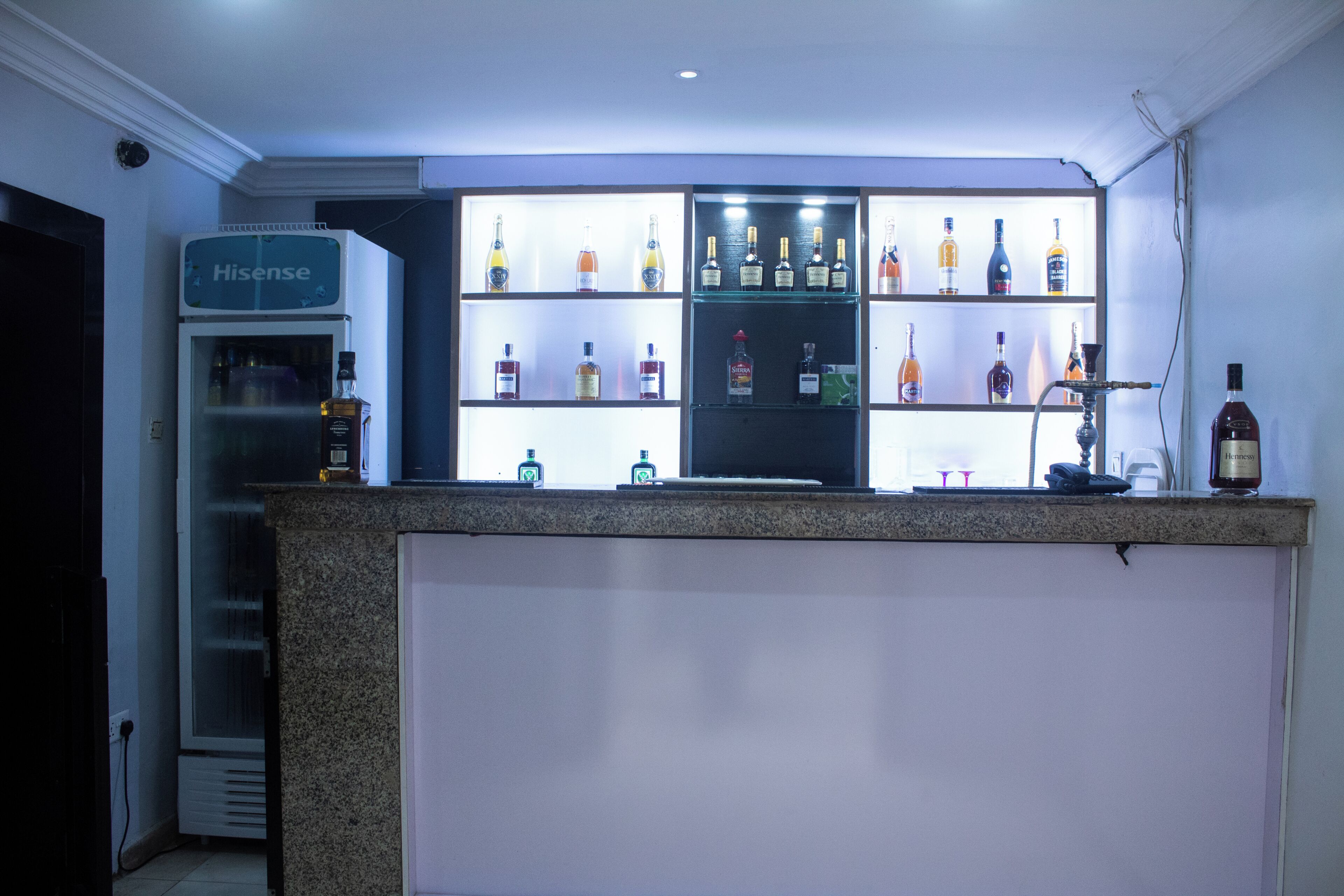 A bar area with shelves of various liquor bottles, a refrigerator, and a coffee machine.