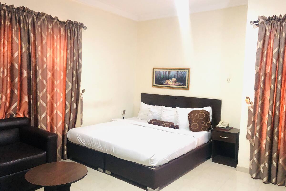 A hotel room with a bed, a nightstand, a chair, and a small table.