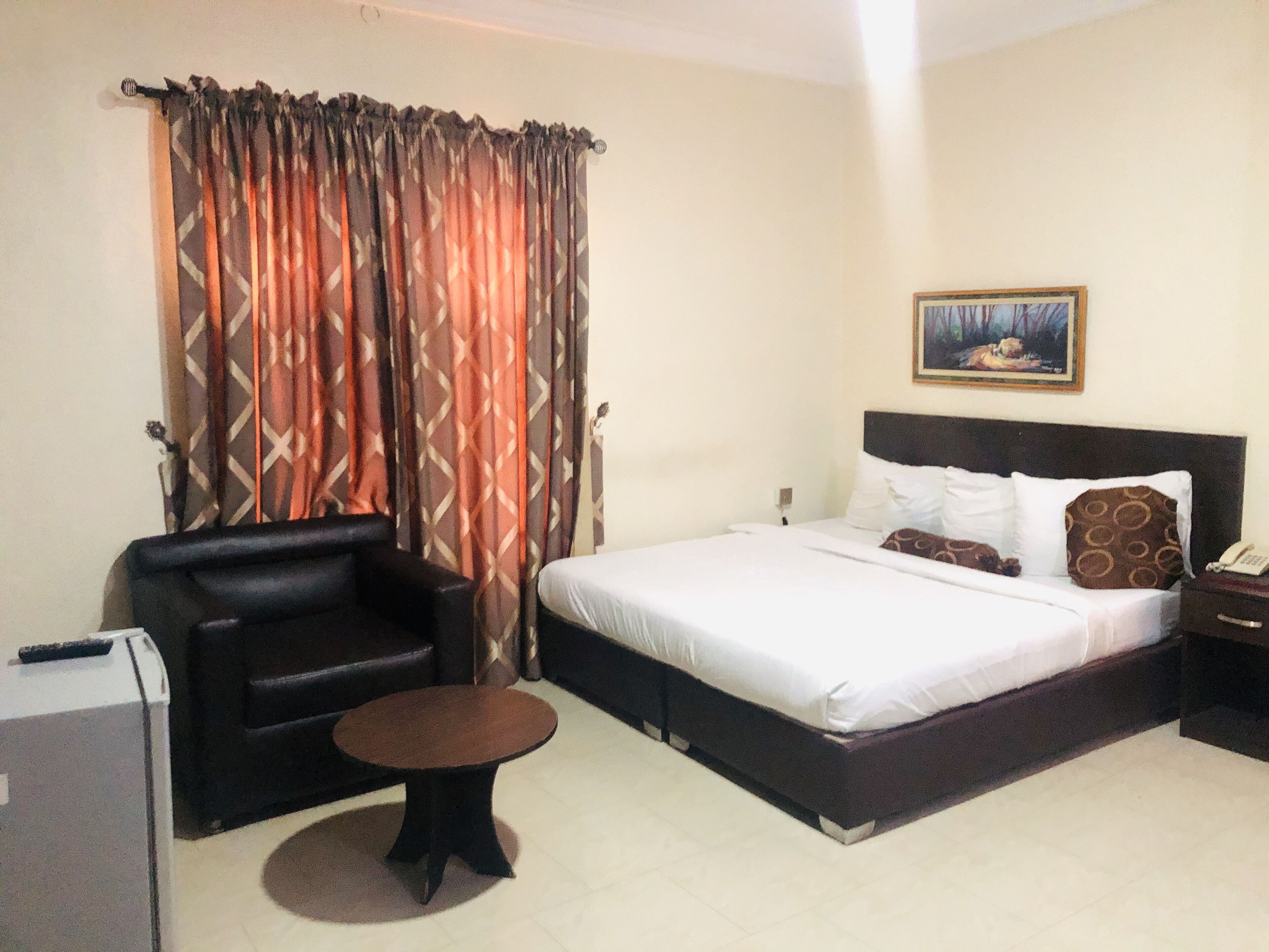 A hotel room with a bed, a small round table, a sofa, and a painting on the wall.