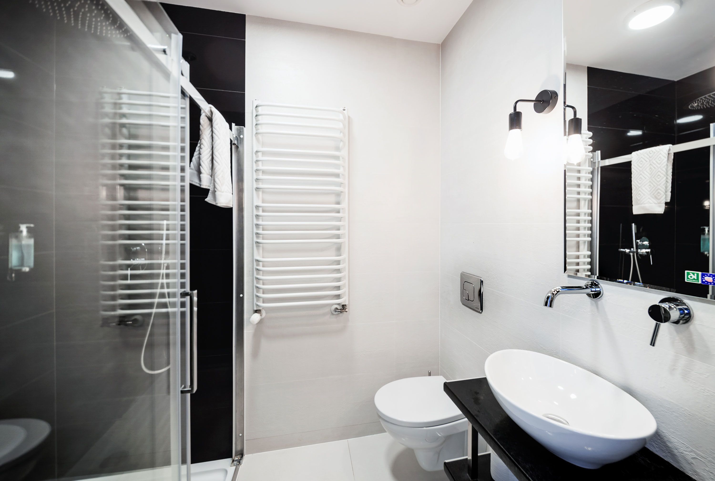 Un baño moderno con cabina de ducha de vidrio, inodoro blanco y encimera negra con lavamanos blanco.