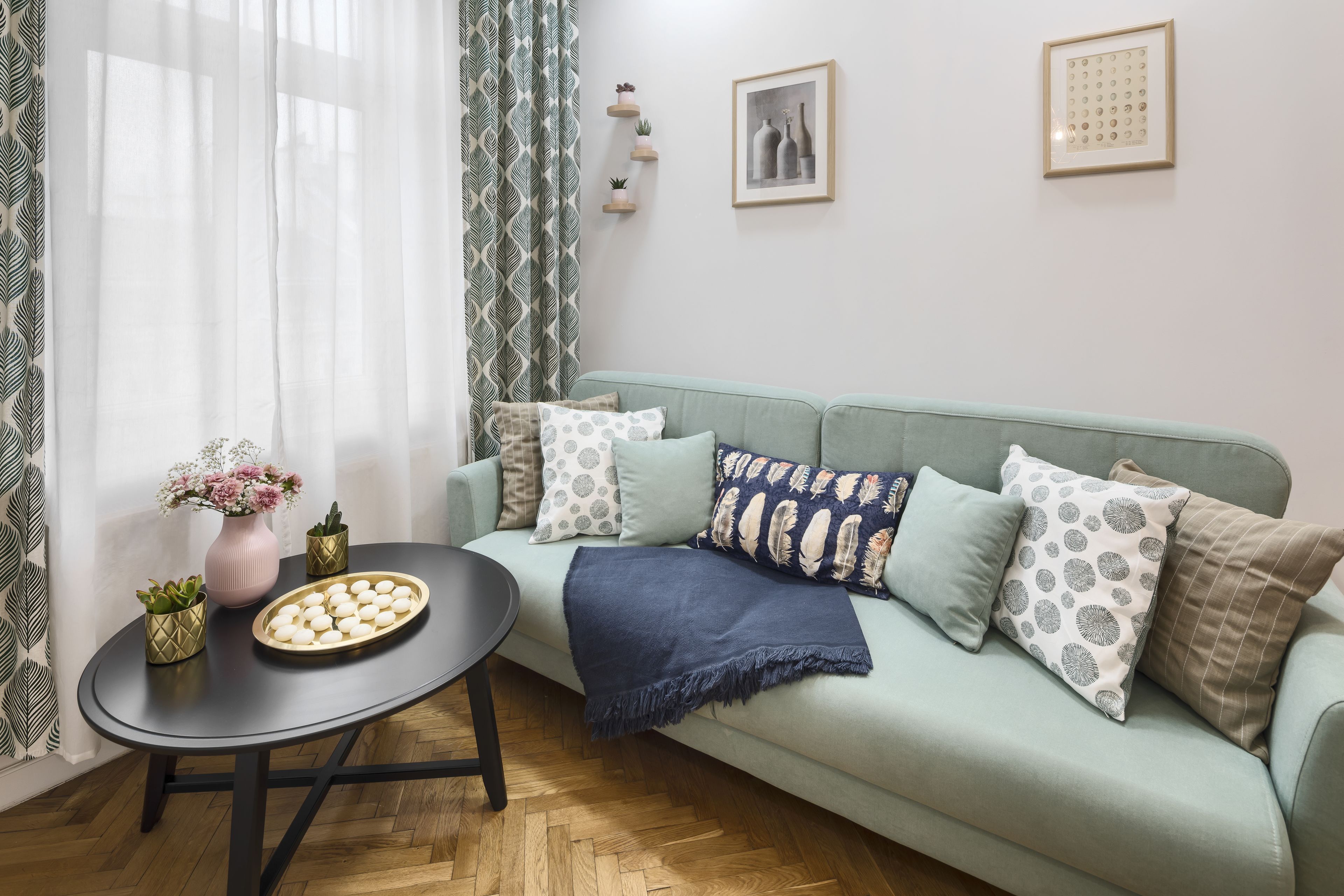A living room with a light green sofa, a round black table, and a vase with flowers.
