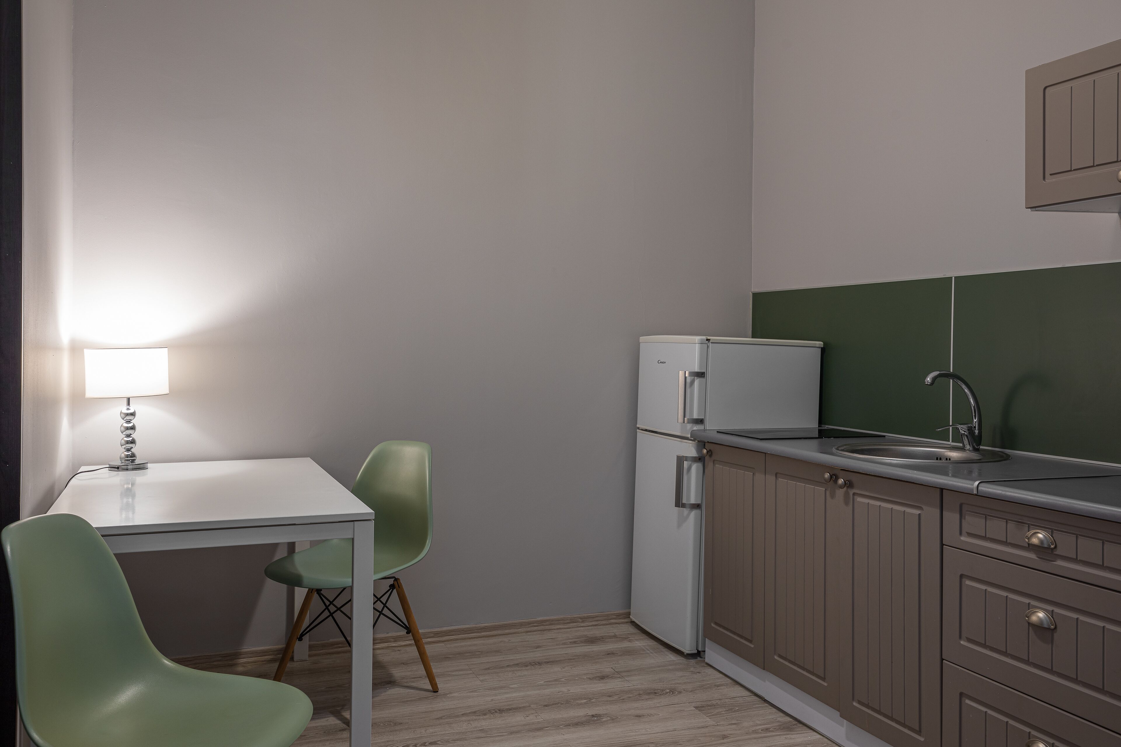 A compact kitchen with a white table, two green chairs, a refrigerator, and a sink.
