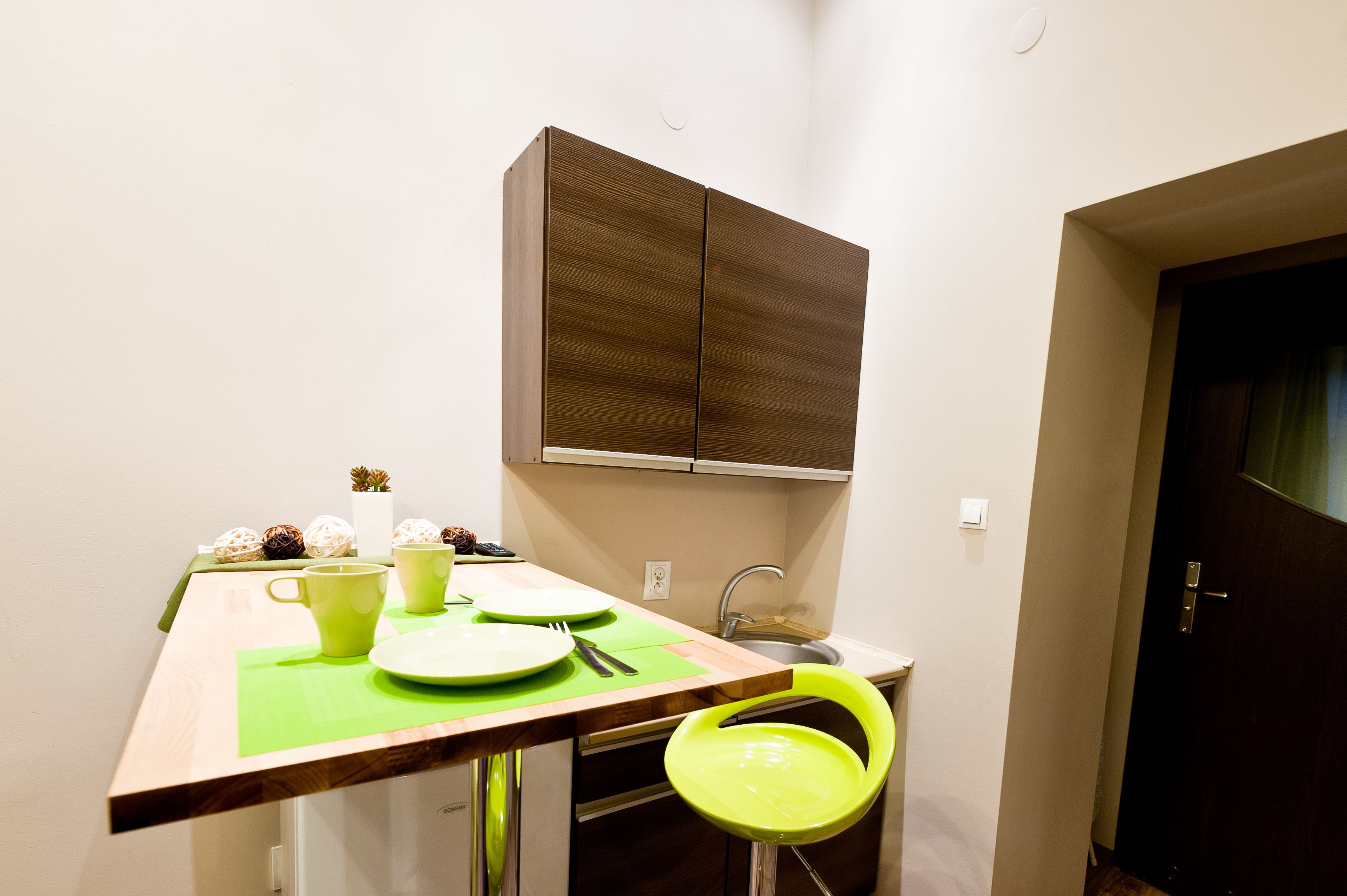 A small kitchen with a wooden table, a green chair, and a cabinet above the sink.