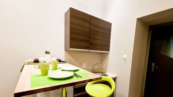 Een kleine keuken met een houten tafel, een groene stoel en een kastje boven de gootsteen.