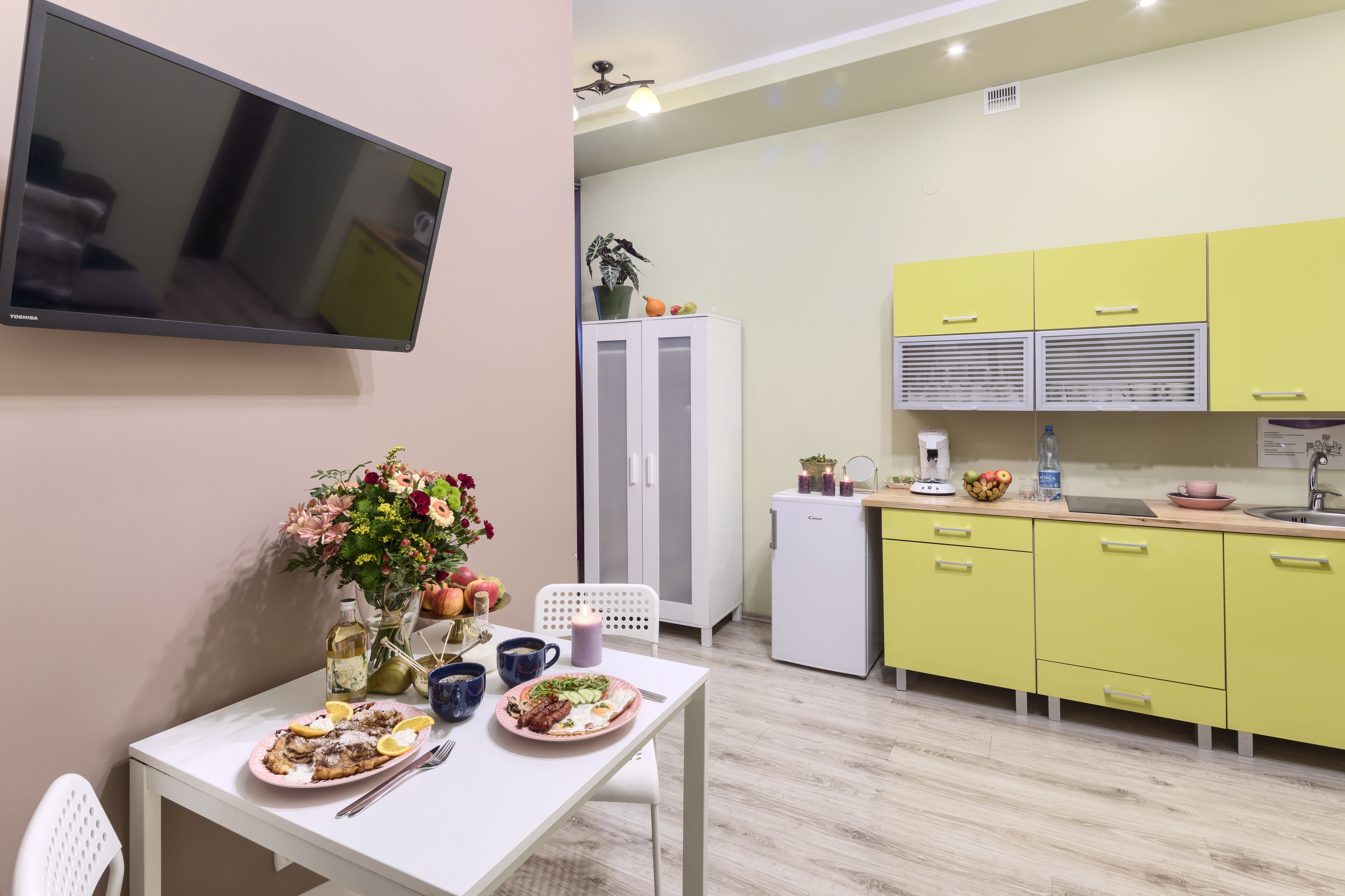 Una cocina moderna con armarios amarillos, un refrigerador blanco y una zona de comedor con una mesa lista para dos.