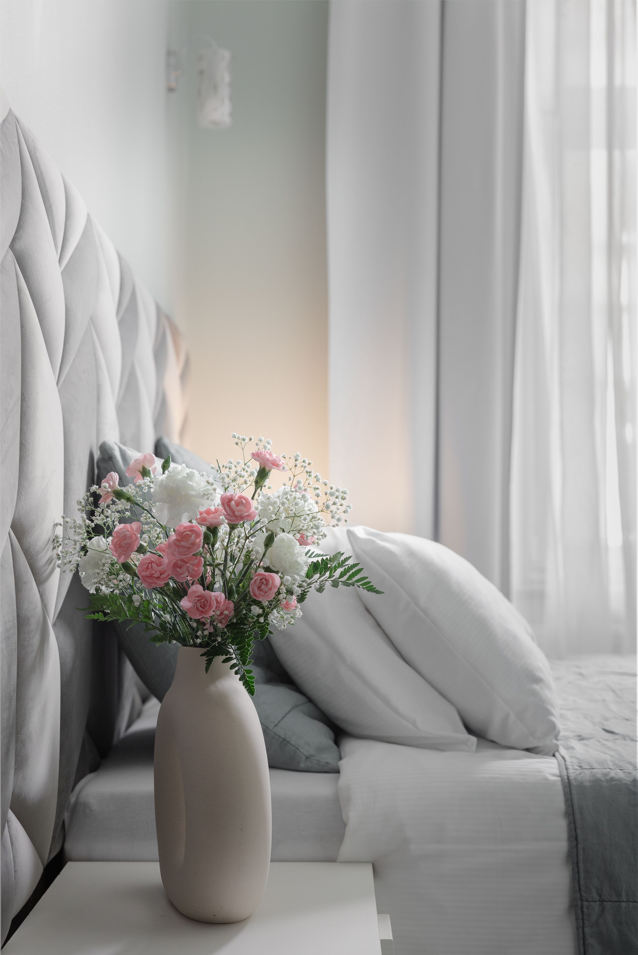 Een slaapkamer met een bed, nachtkastje en een vaas met bloemen.