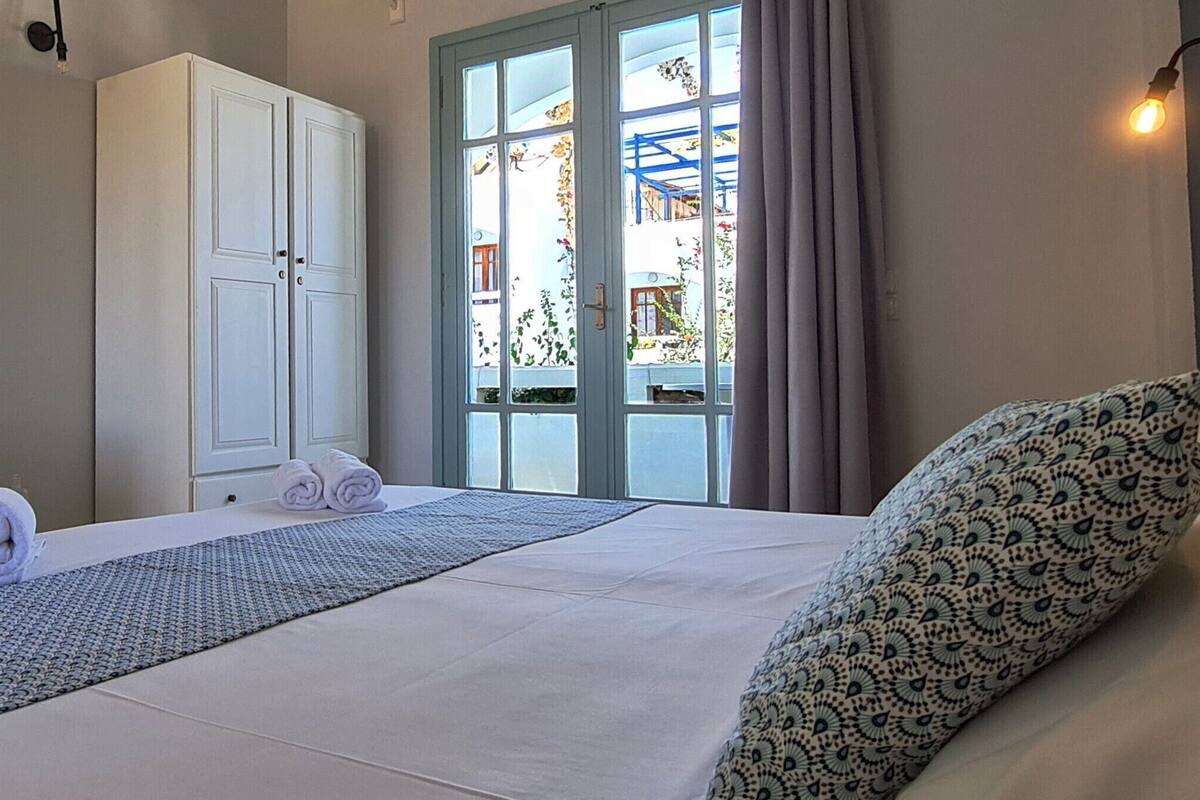 A hotel room with a bed, a bench, a wardrobe, and a window with curtains.